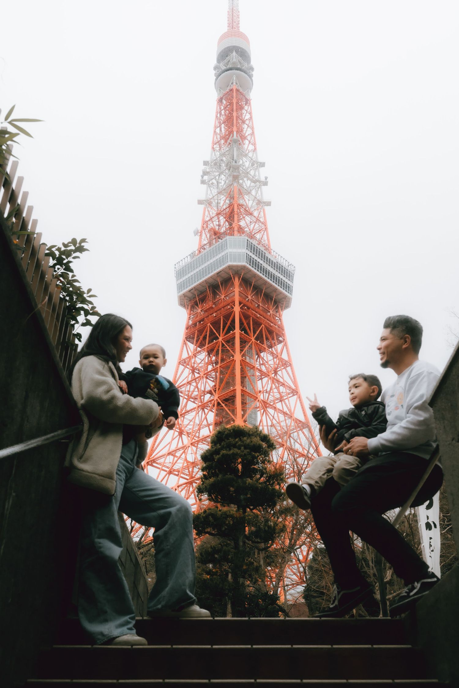 Family of four posing on steps with Tokyo Tower in the background on a misty day in Japan.