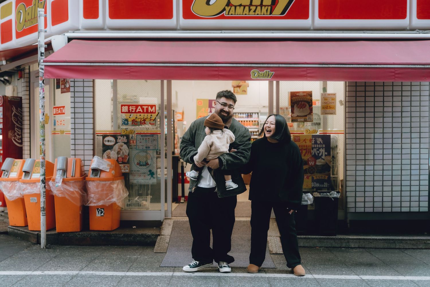 Happy family with baby posing outside a Japanese convenience store in shinkyuku, tokyo.