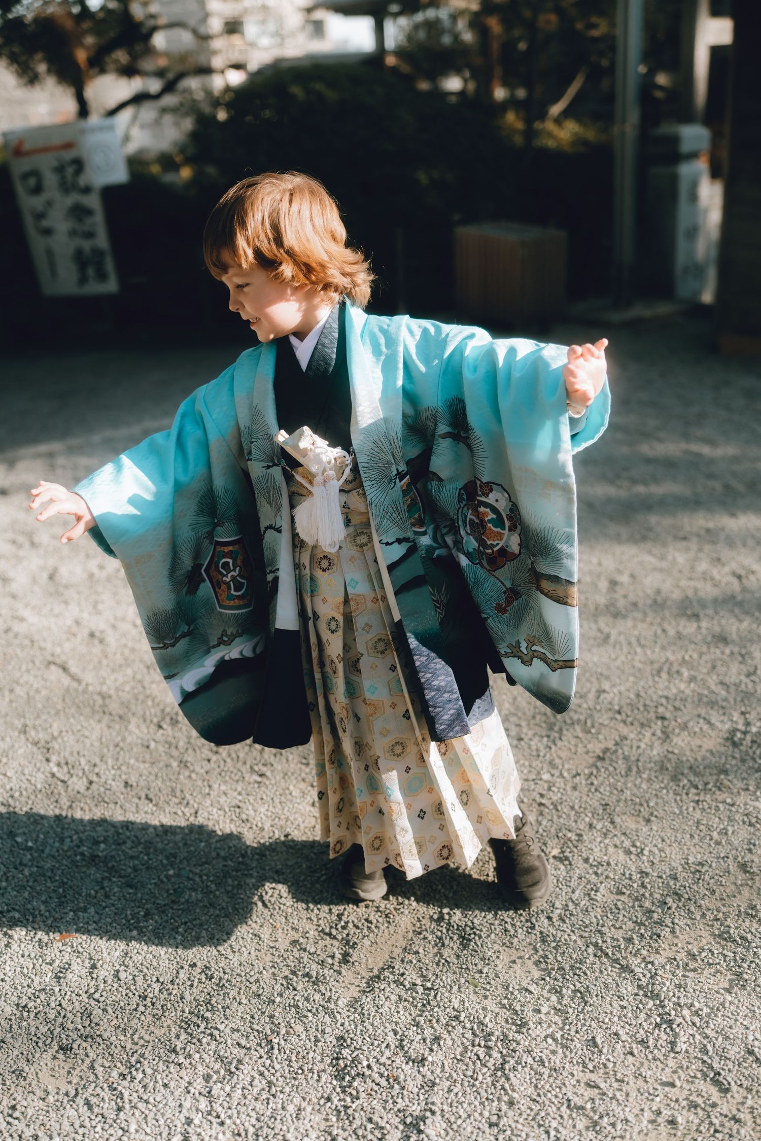 Young child wearing a traditional Japanese kimono at a yokohama shrine, smiling and walking on gravel path.