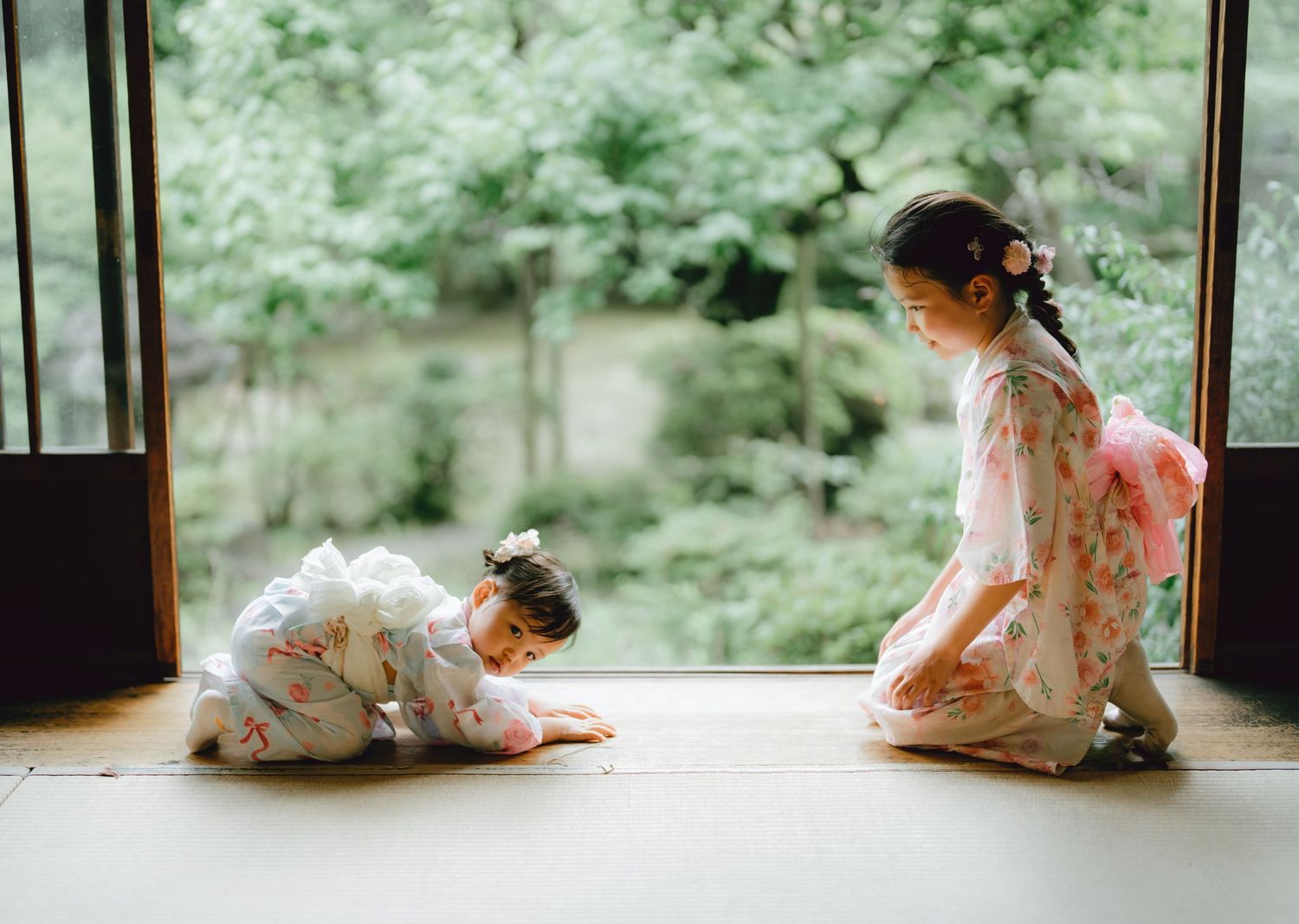 Toddlers in traditional Japanese kimonos sitting on a tatami floor near an open shoji door overlooking a lush garden in kawagoe.