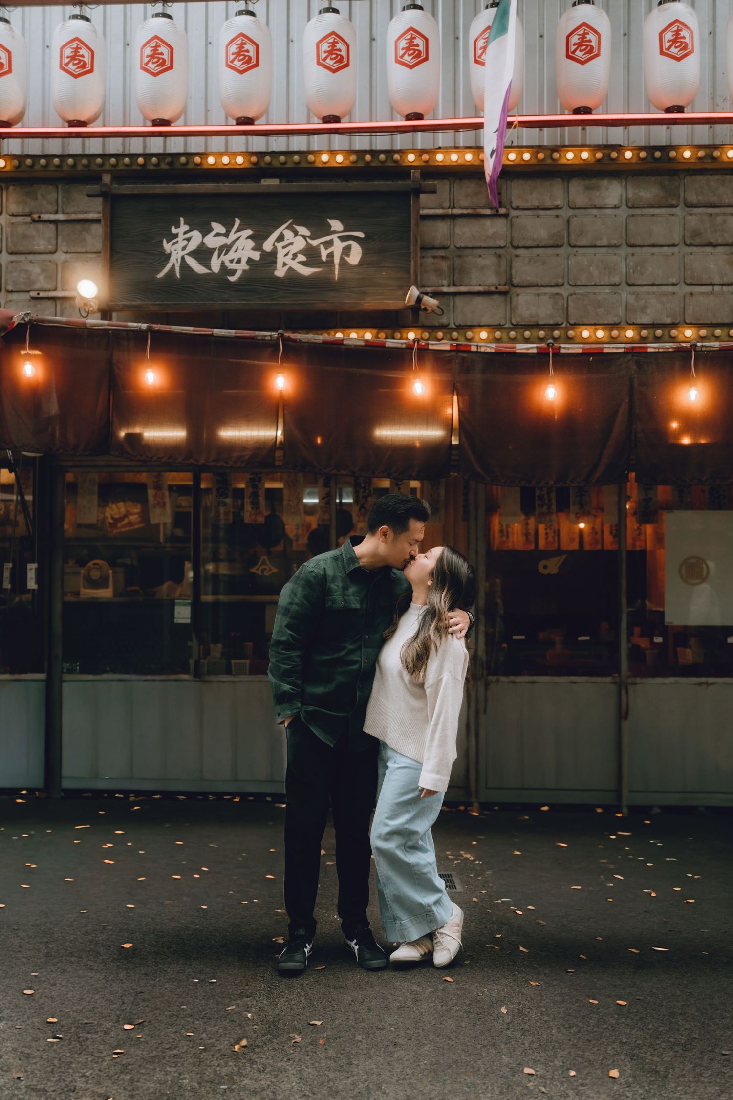 Couple sharing a romantic kiss in front of a warmly lit Japanese restaurant at dusk in shibuyayokocho, shibuya,  tokyo.