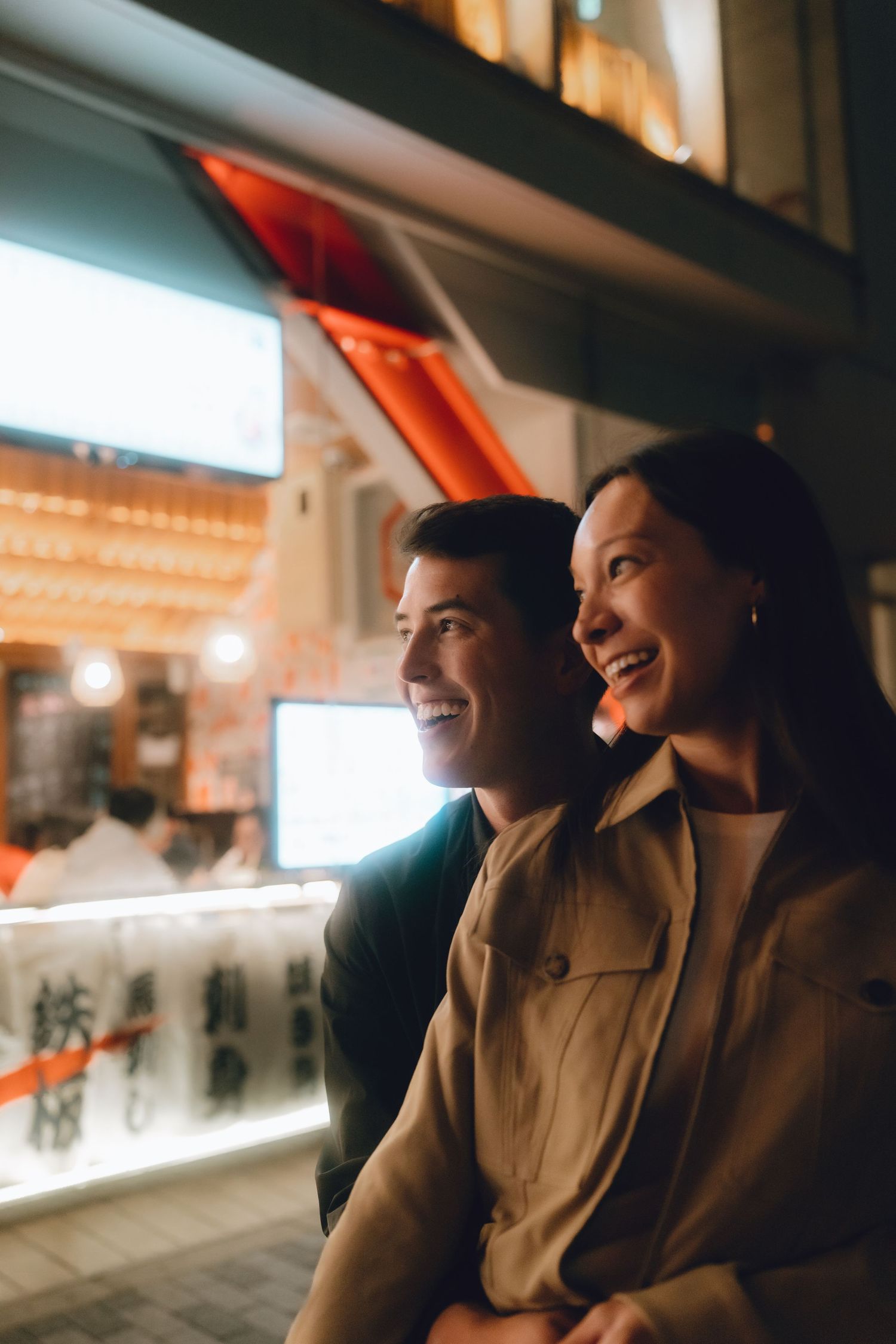 A smiling couple enjoys a night out together near illuminated Asian restaurant signs in yurakucho, tokyo.
