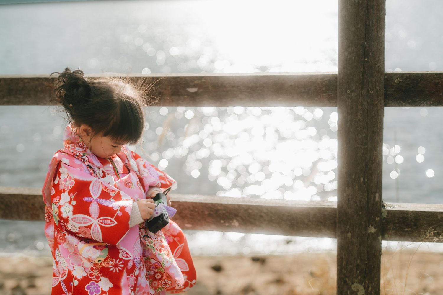Young girl in a red floral kimono stands by a wooden railing, looking down near lake yamanaka.
