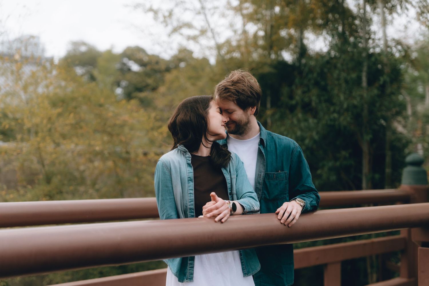 A young couple sharing a romantic moment on a wooden bridge surrounded by autumn trees.