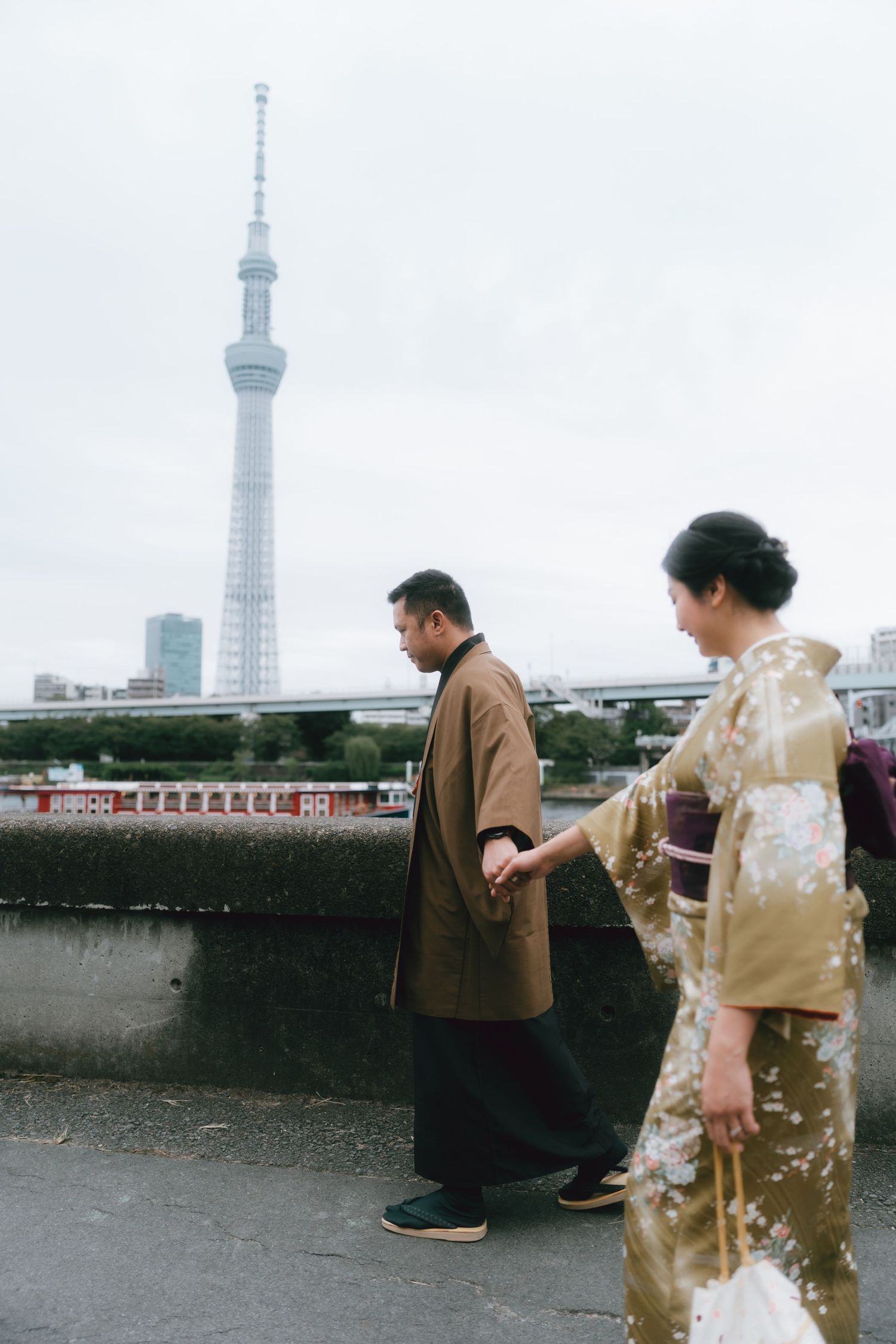 Couple in traditional Japanese kimono walking near Tokyo Skytree on an overcast day.