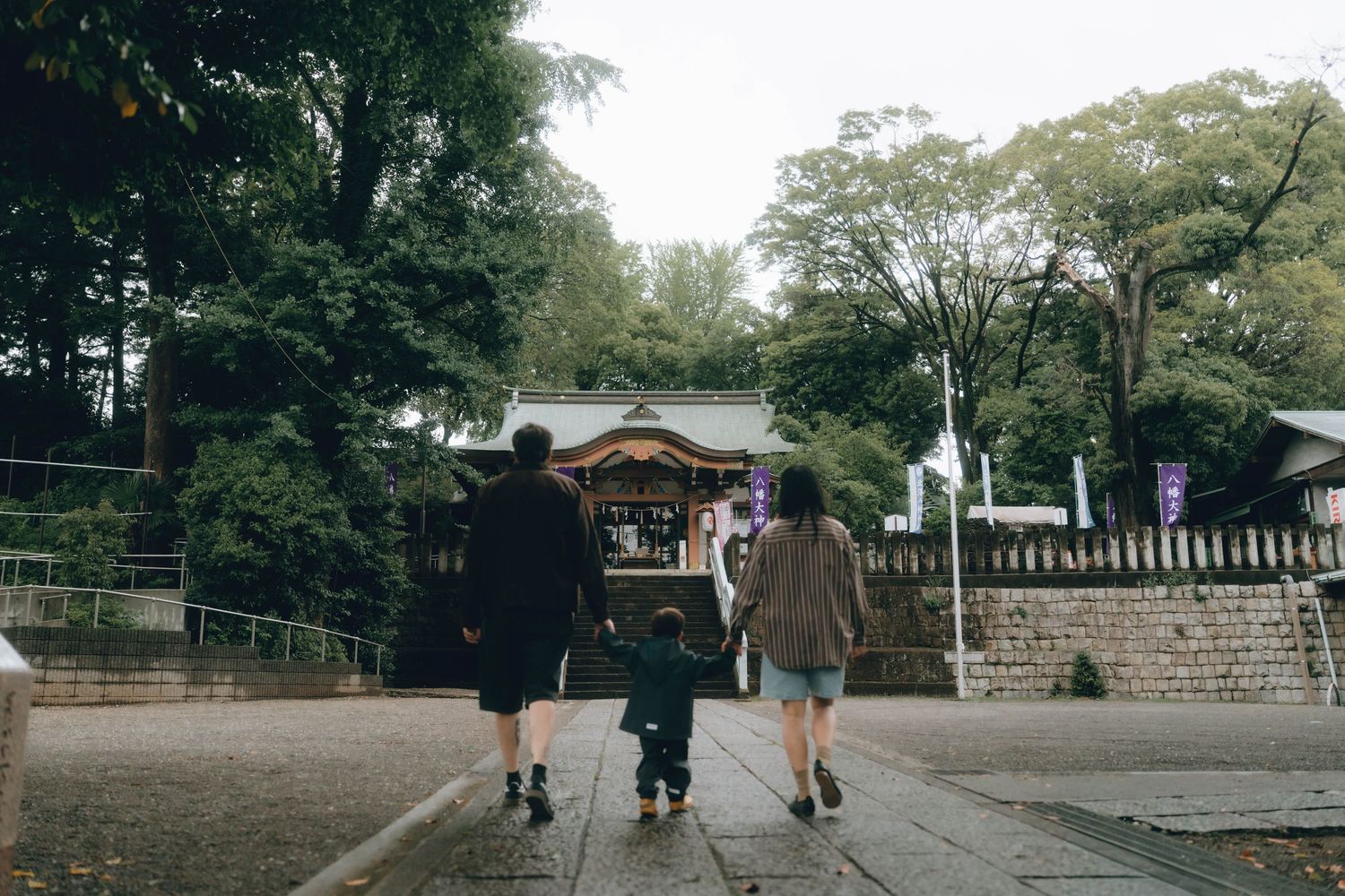 Two people stand smiling in front of a traditional Japanese shrine while a child stands in the foreground in Shimokitazawa, TOKYO.
