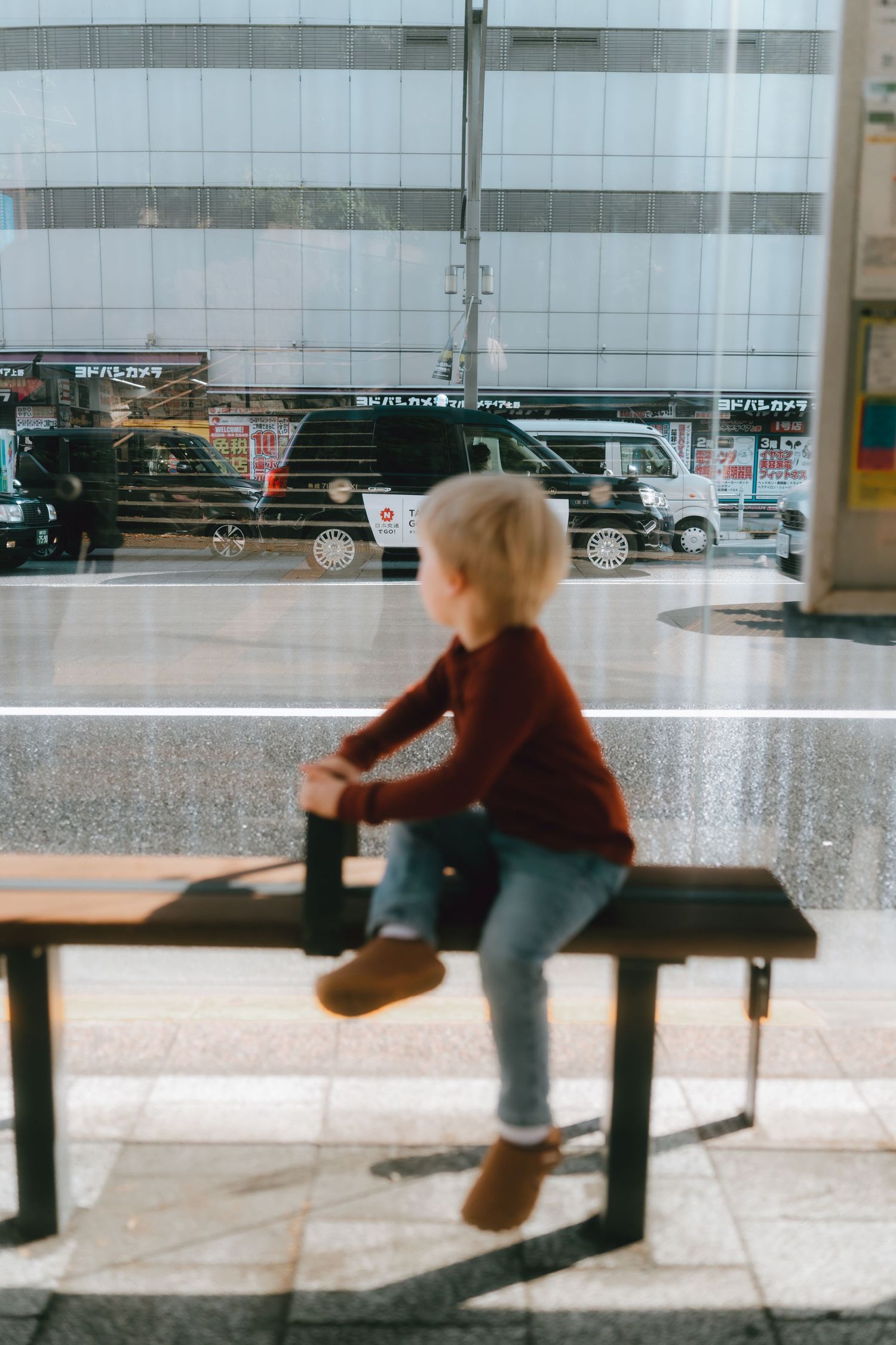 Blonde child sitting on a bench inside a modern building in ueno, tokyo.