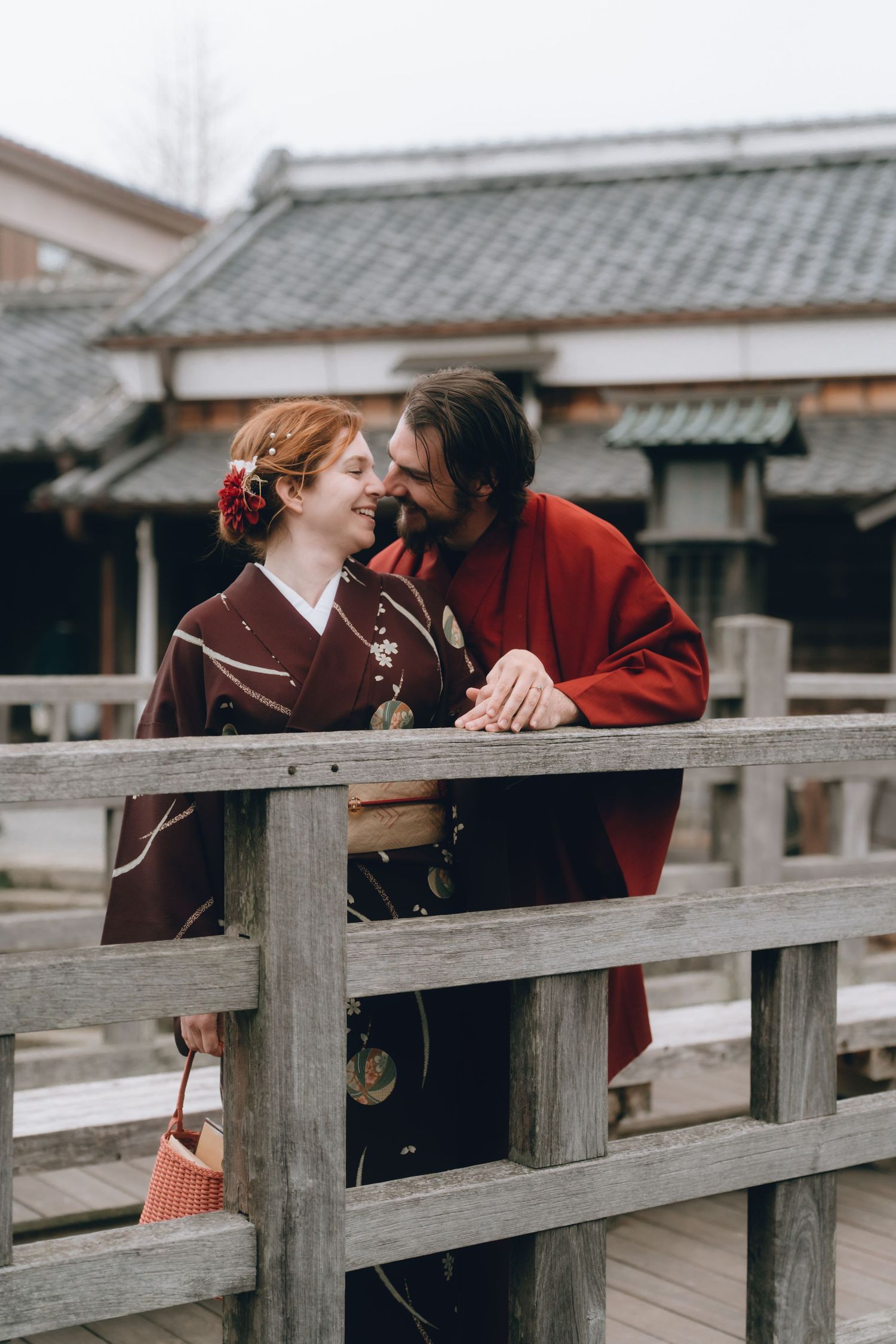 Couple in traditional Japanese kimono smiling on a wooden bridge with historic buildings in the background. in Sawara, Chiba, Japan.