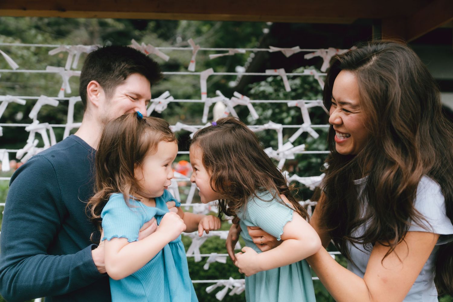 A happy family with two young girls in blue dresses laughing together outdoors at a playground in Zojoji, Tokyo.