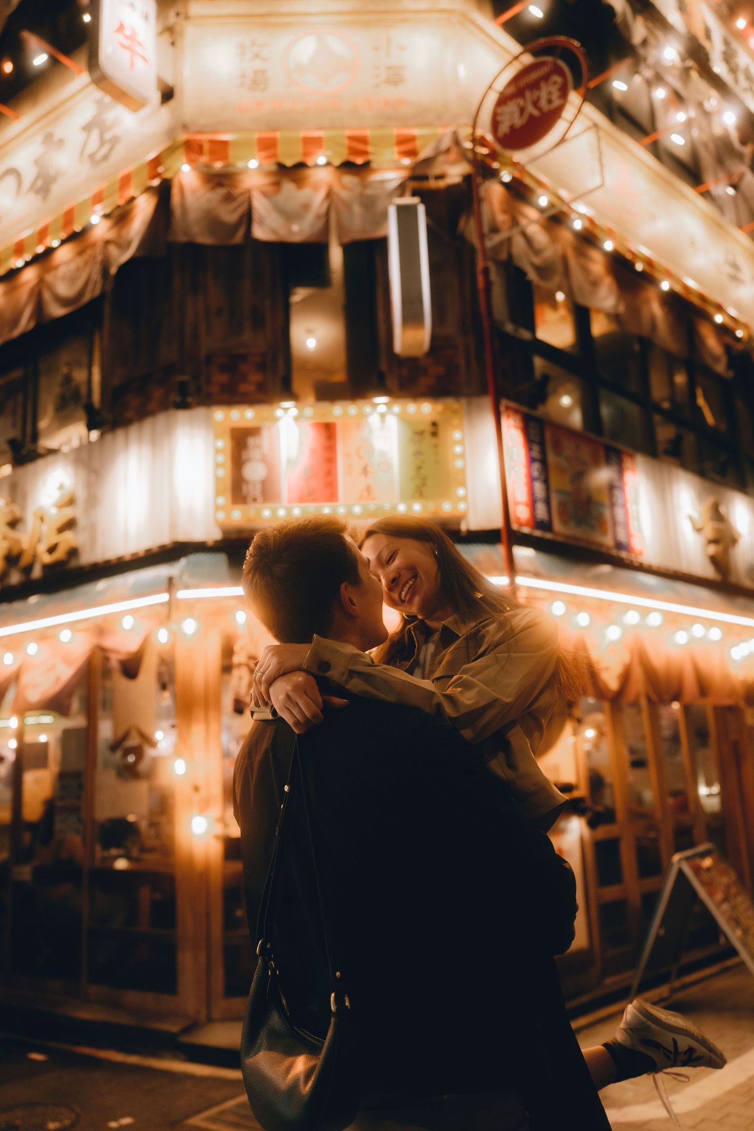 Couple embracing and smiling outside a warmly lit Japanese restaurant at night.