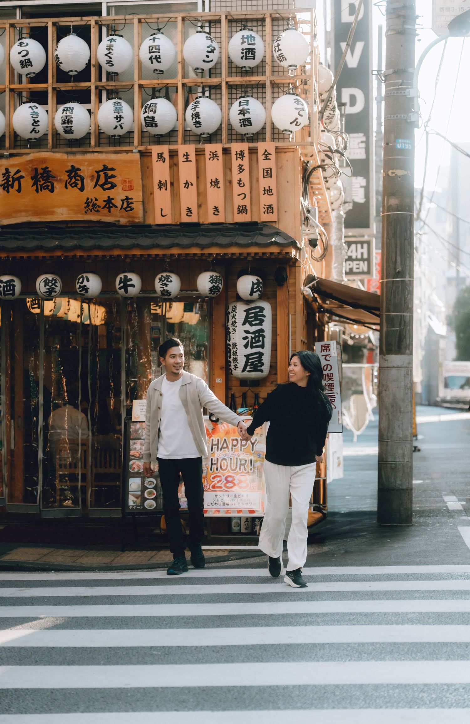Couple holding hands and smiling outside a traditional Japanese izakaya with paper lanterns in Tokyo.