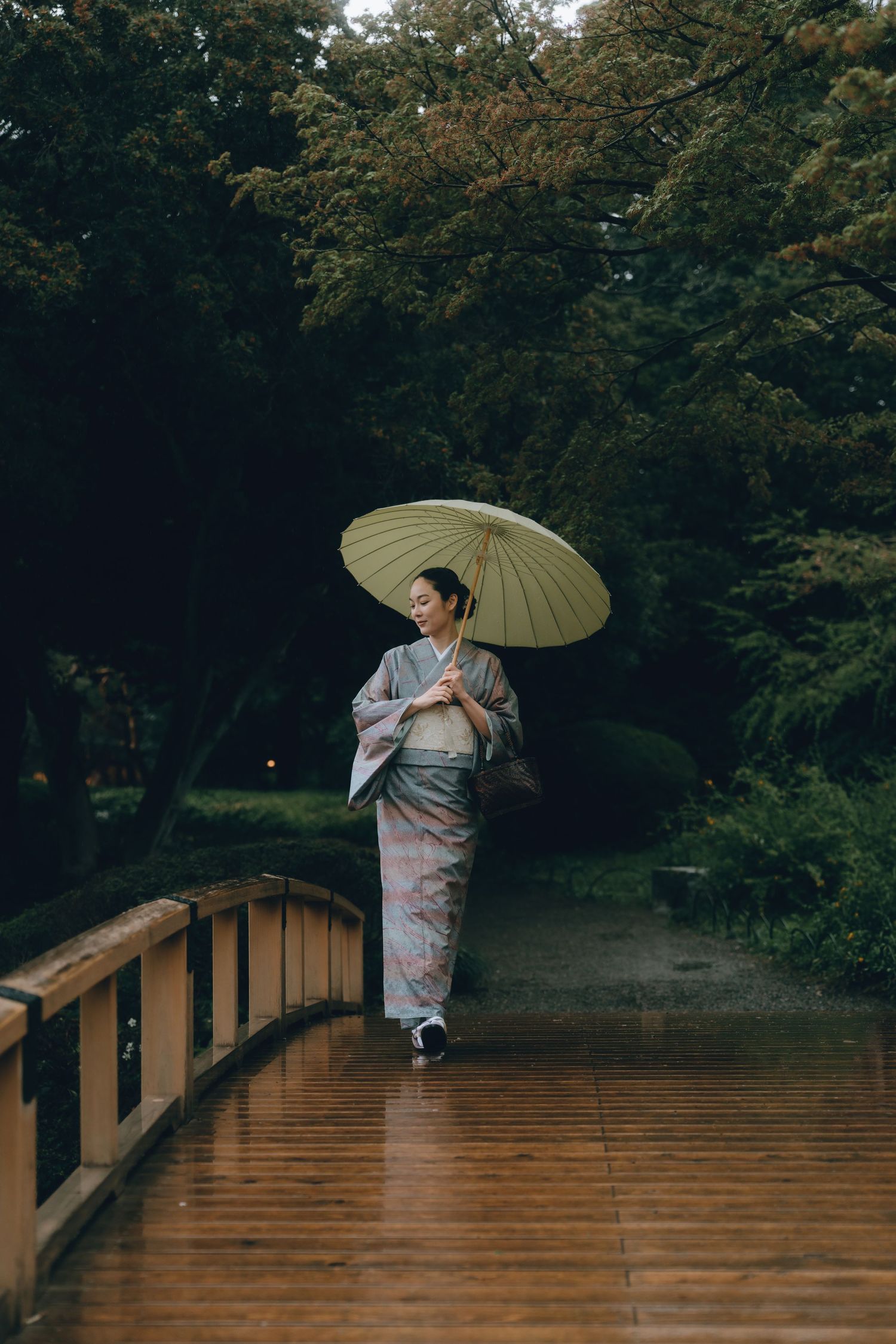 A woman in a traditional Japanese kimono walks on a wooden bridge holding a parasol umbrella in shinjyuku gyoen, tokyo.