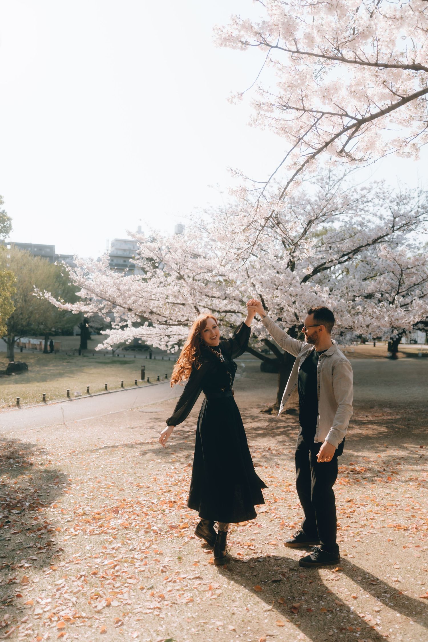 Couple dancing under blooming cherry blossom trees in sumida park during spring, with pink petals on the ground.