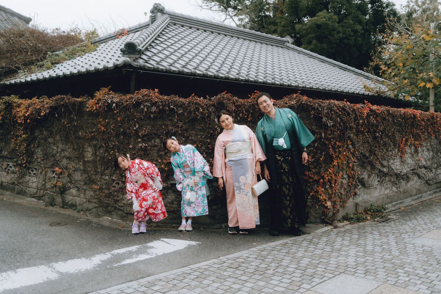 Four women in colorful traditional Japanese kimonos posing in front of a stone wall with autumn ivy in kawagoe, Japan.