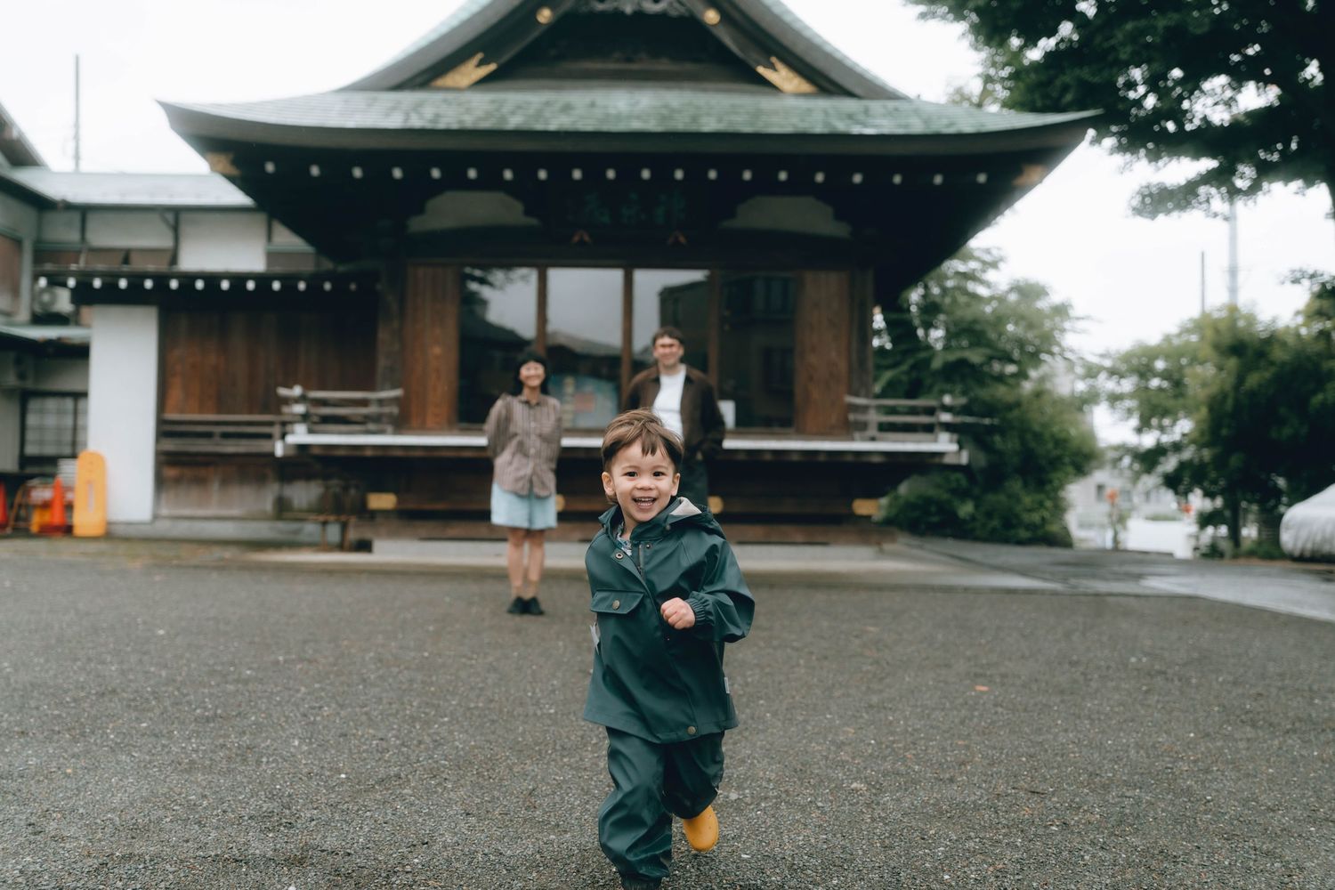 Two people stand smiling in front of a traditional Japanese shrine while a child stands in the foreground in Shimokitazawa, TOKYO.