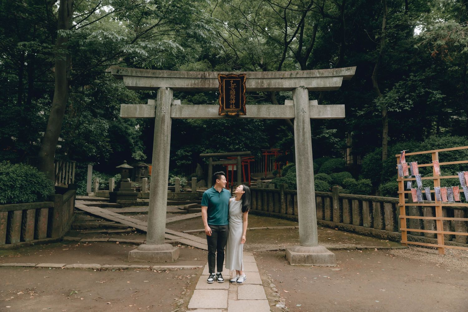 Couple posing together in front of a traditional Japanese torii gate at a serene Shinto shrine surrounded by trees.