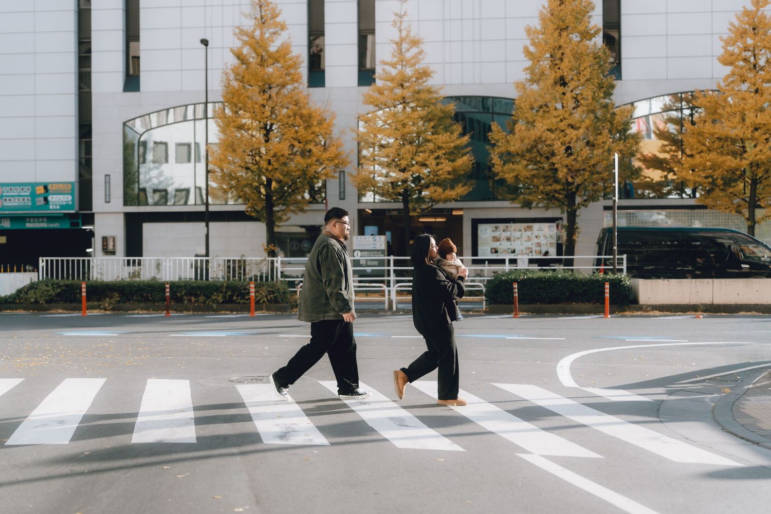 family walking across a zebra crossing in an urban area with autumn trees and a modern building backdrop in Shinjyuku, Tokyo.