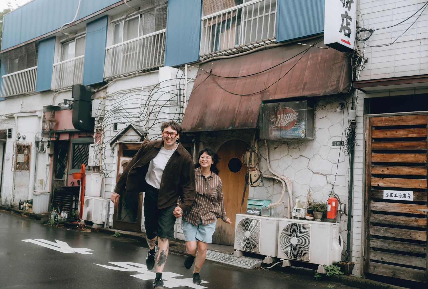 Couple walking and laughing on a rainy street in shimokitazawa,tokyo, passing colorful storefronts in an urban neighborhood.