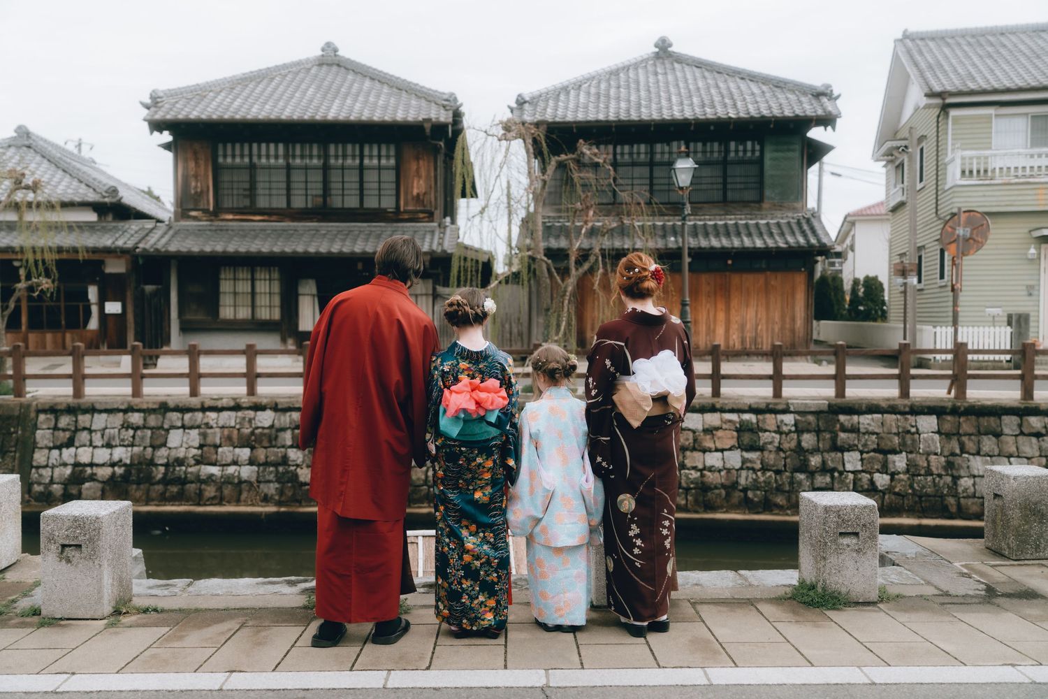 Family of four wearing traditional Japanese kimonos standing together by a canal with historic buildings in Sawara, Chiba, Japan.