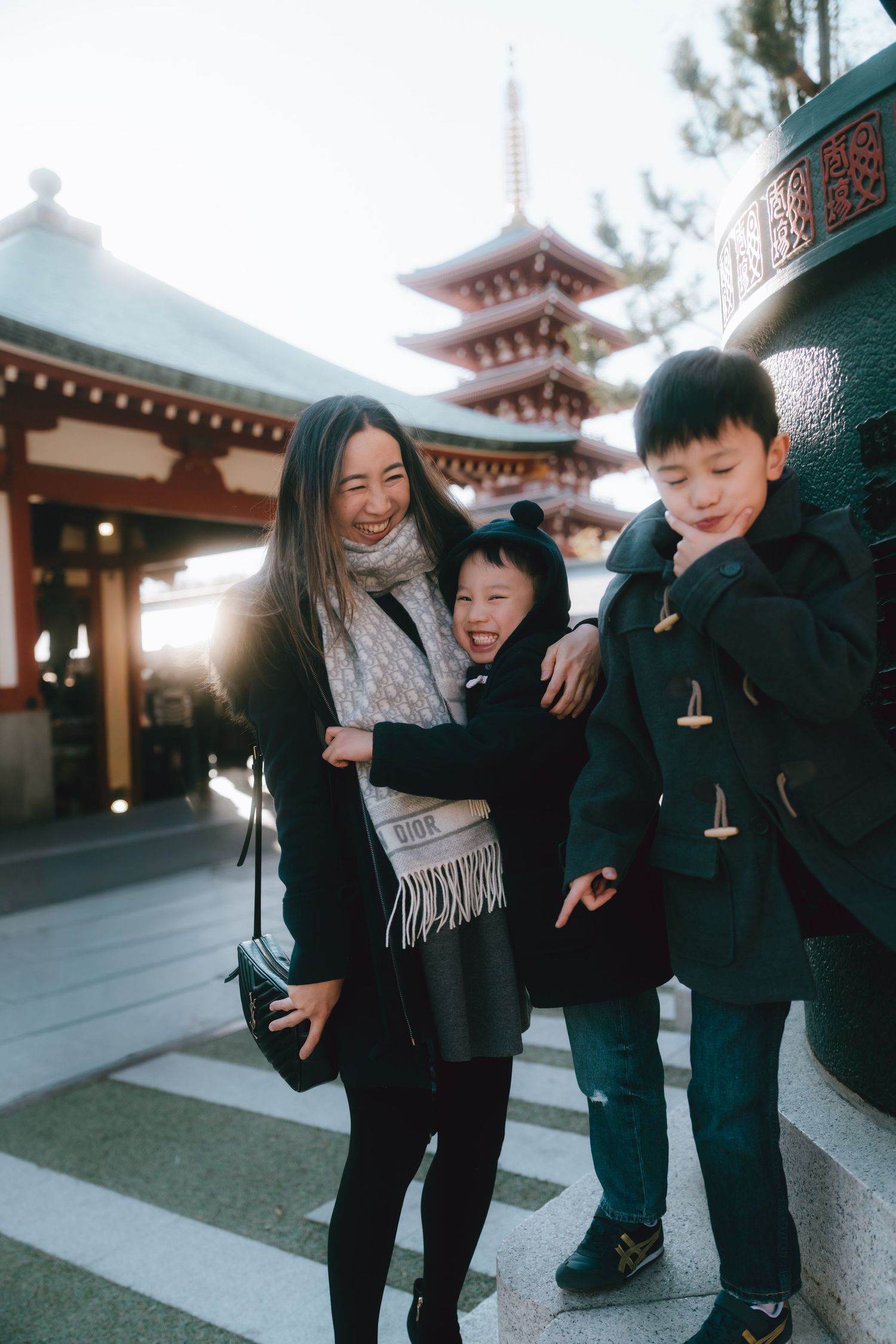 A smiling Asian family with a mother and two children posing near a pagoda at Senso-ji Temple in Tokyo.