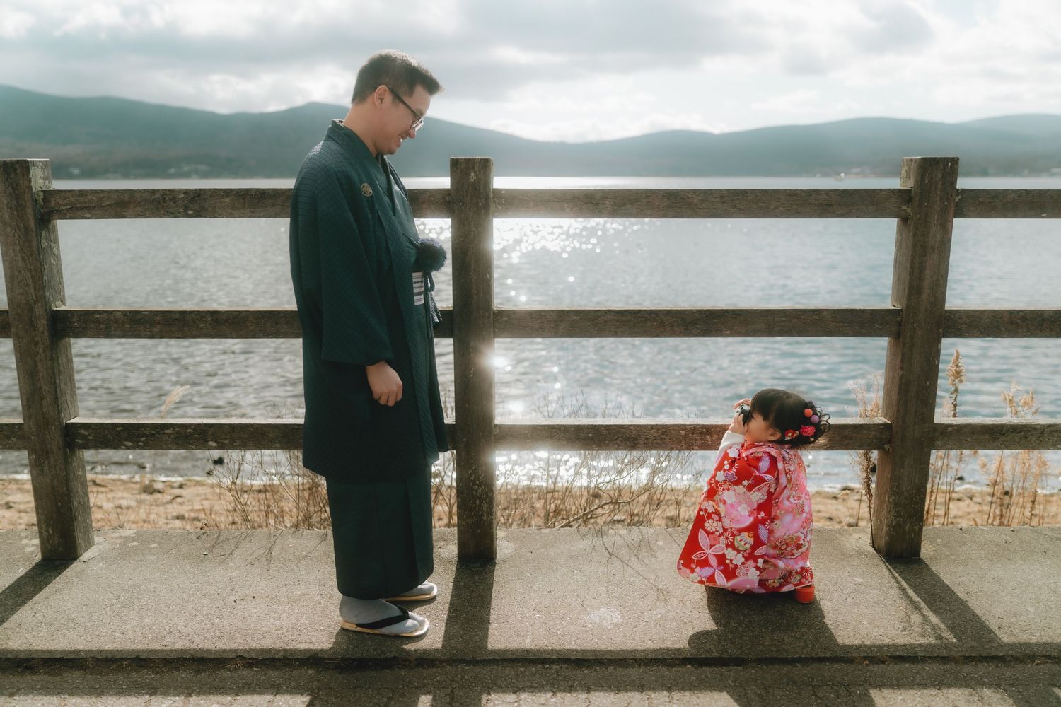 Family in traditional Japanese kimonos walking along a lakeside promenade with Mount Fuji in the background in Lake Yamanaka.