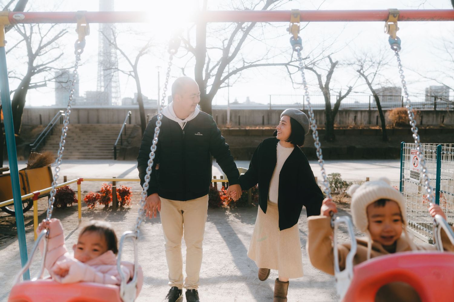Elderly couple holding hands at a Sumida park while two young children play on swings on a sunny day in Asakusa Tokyo.