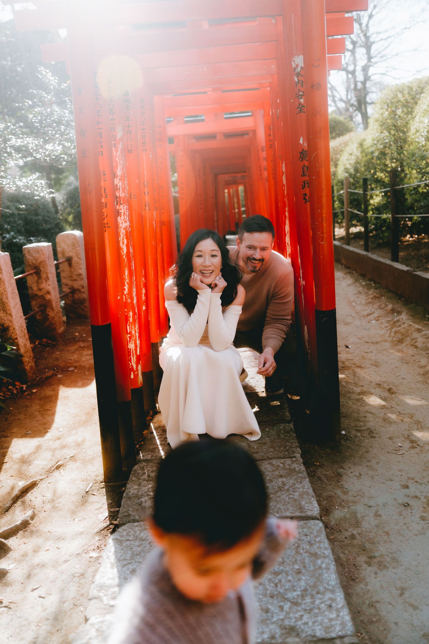 Couple smiling under red torii gates at Nezu shrine, Tokyo. , with a child in the foreground