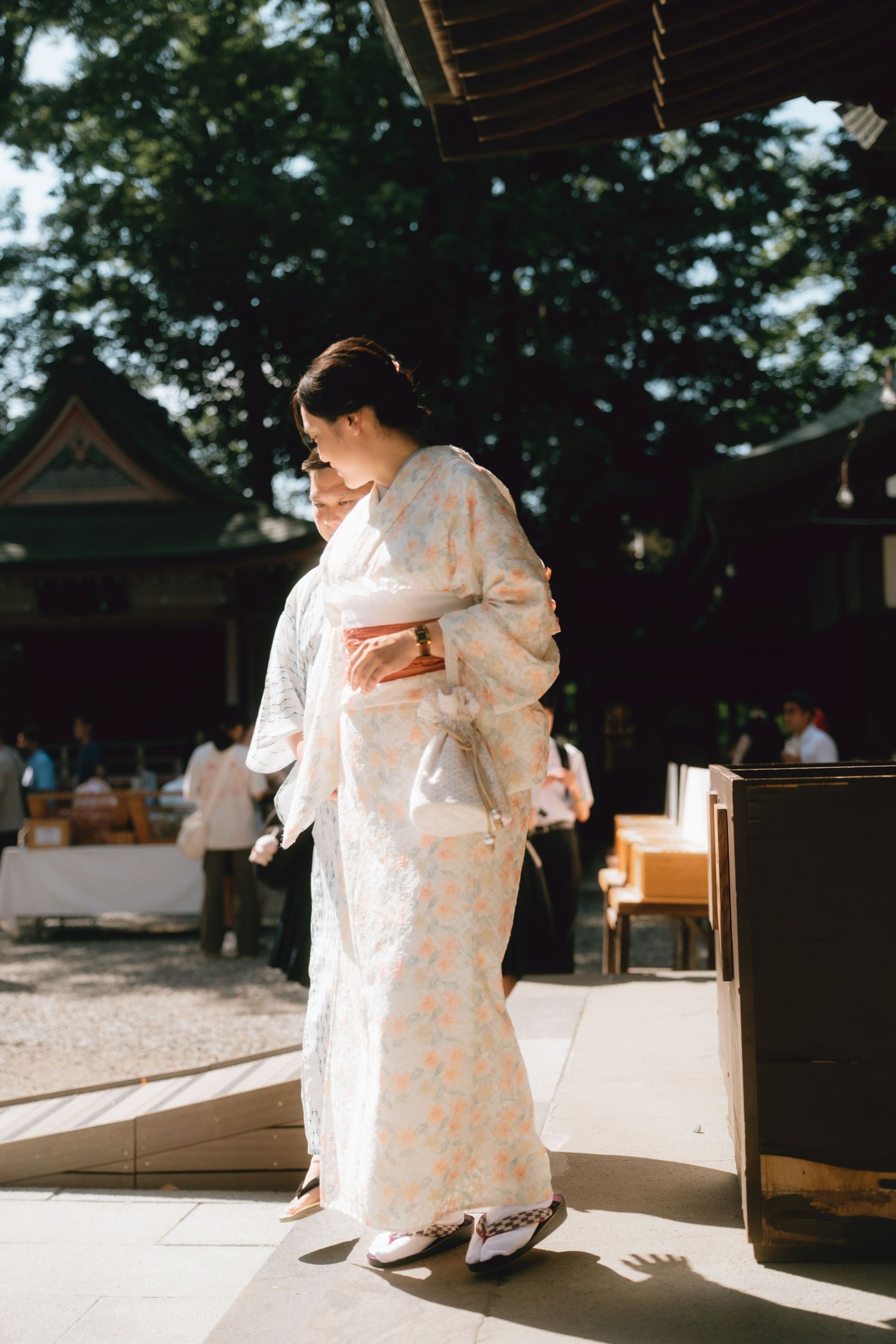 A woman in a traditional white floral kimono walks gracefully at a Japanese shrine surrounded by trees in Hikawa shrine, Kawagoe.