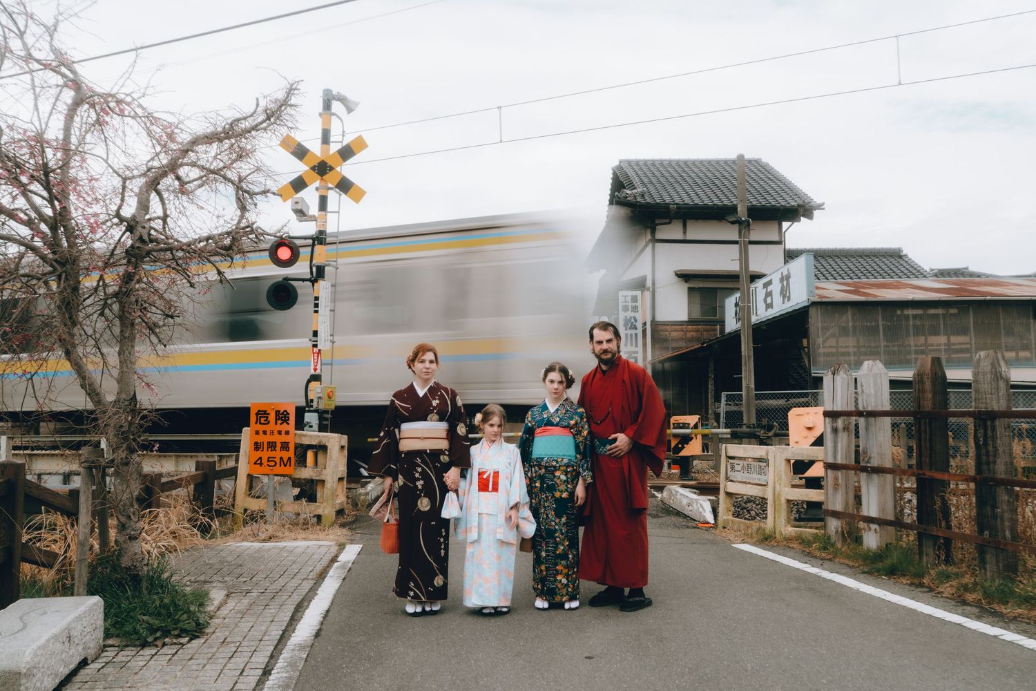 Family of four in traditional Japanese kimono posing at a railroad crossing with a passing train in Sawara, Chiba, Japan.