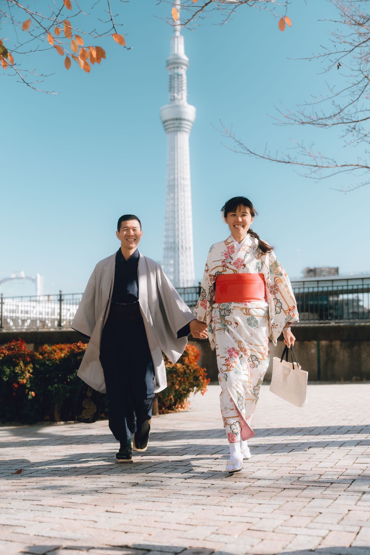 Couple in traditional Japanese kimono and hakama walking hand in hand with Tokyo Skytree in background.