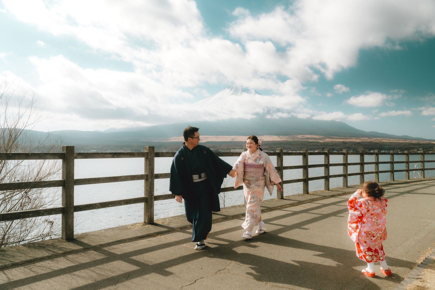 Family in traditional Japanese kimonos walking along a lakeside promenade with Mount Fuji in the background in Lake Yamanaka.