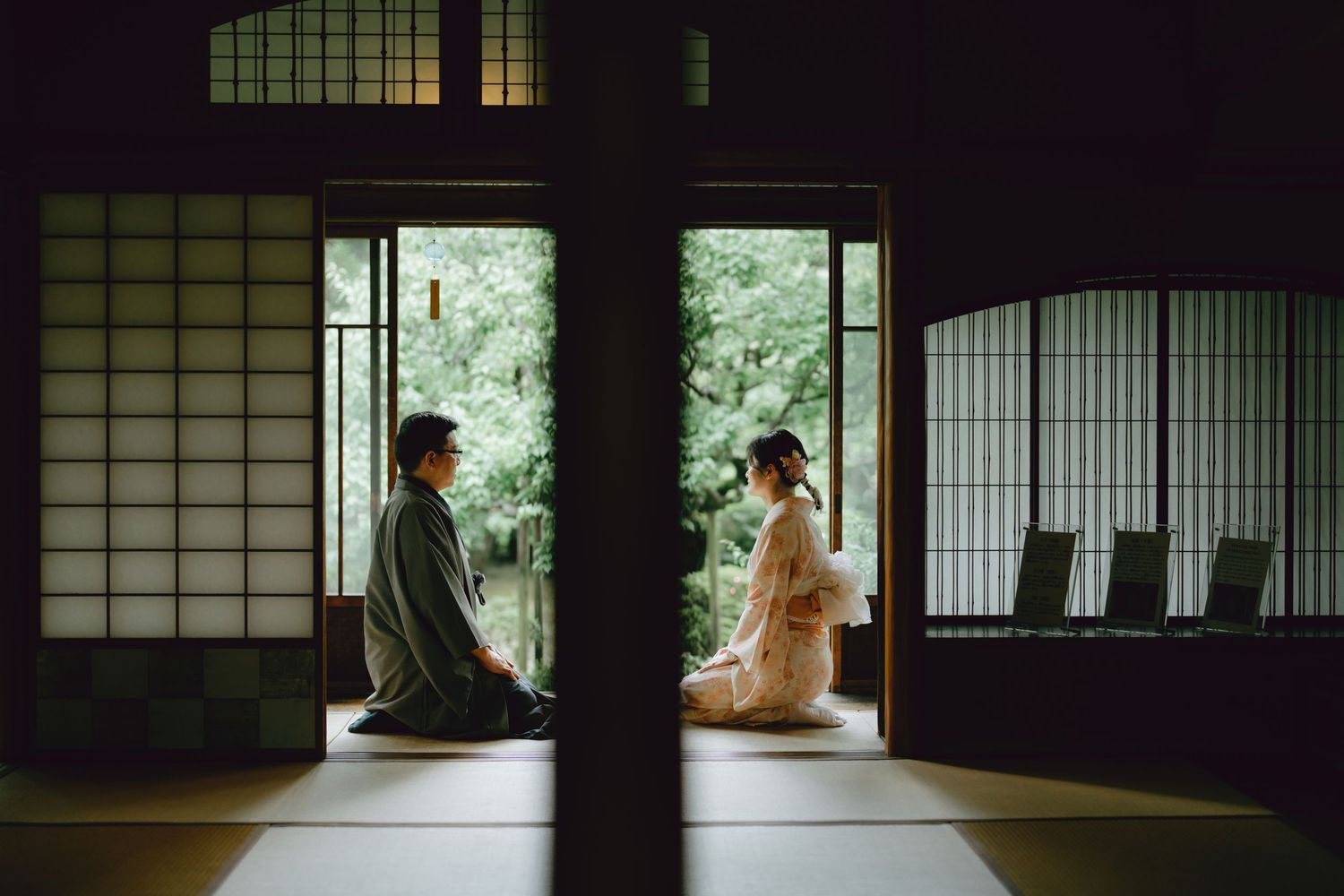 A couple in traditional Japanese kimono sit facing each other in a serene tatami room with shoji screens.