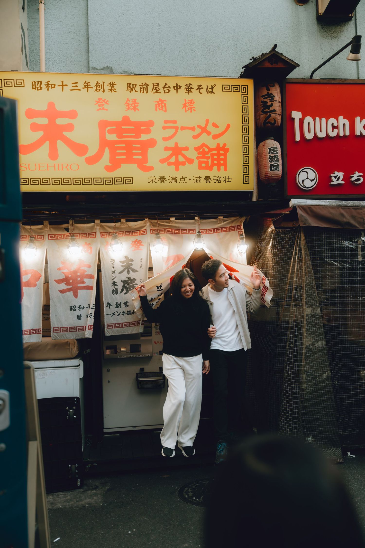 Couple embracing outside a traditional ramen restaurant at night in Shinbashi, Tokyo.