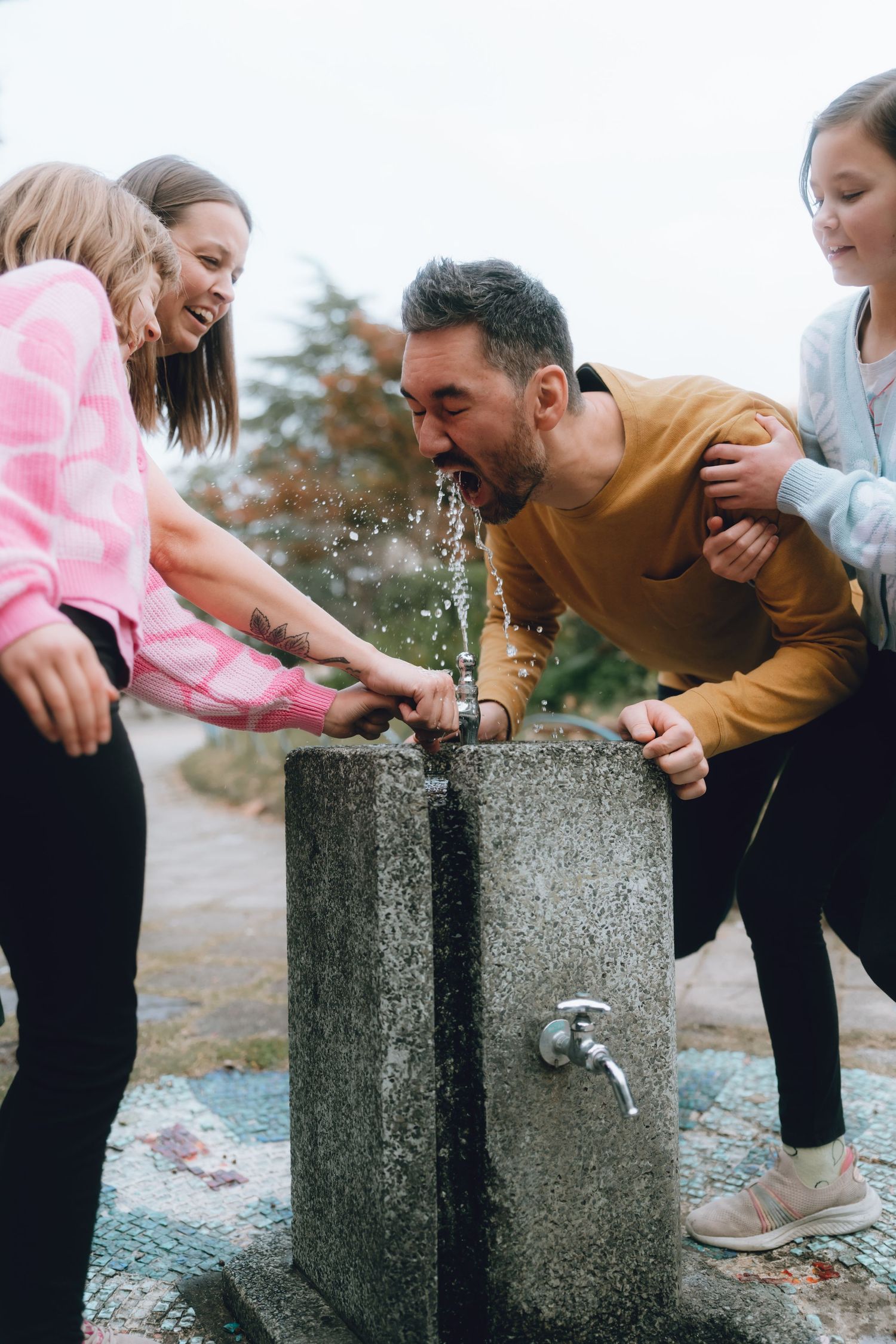 Man drinking from stone water fountain surrounded by laughing children outdoors in Tokyo.