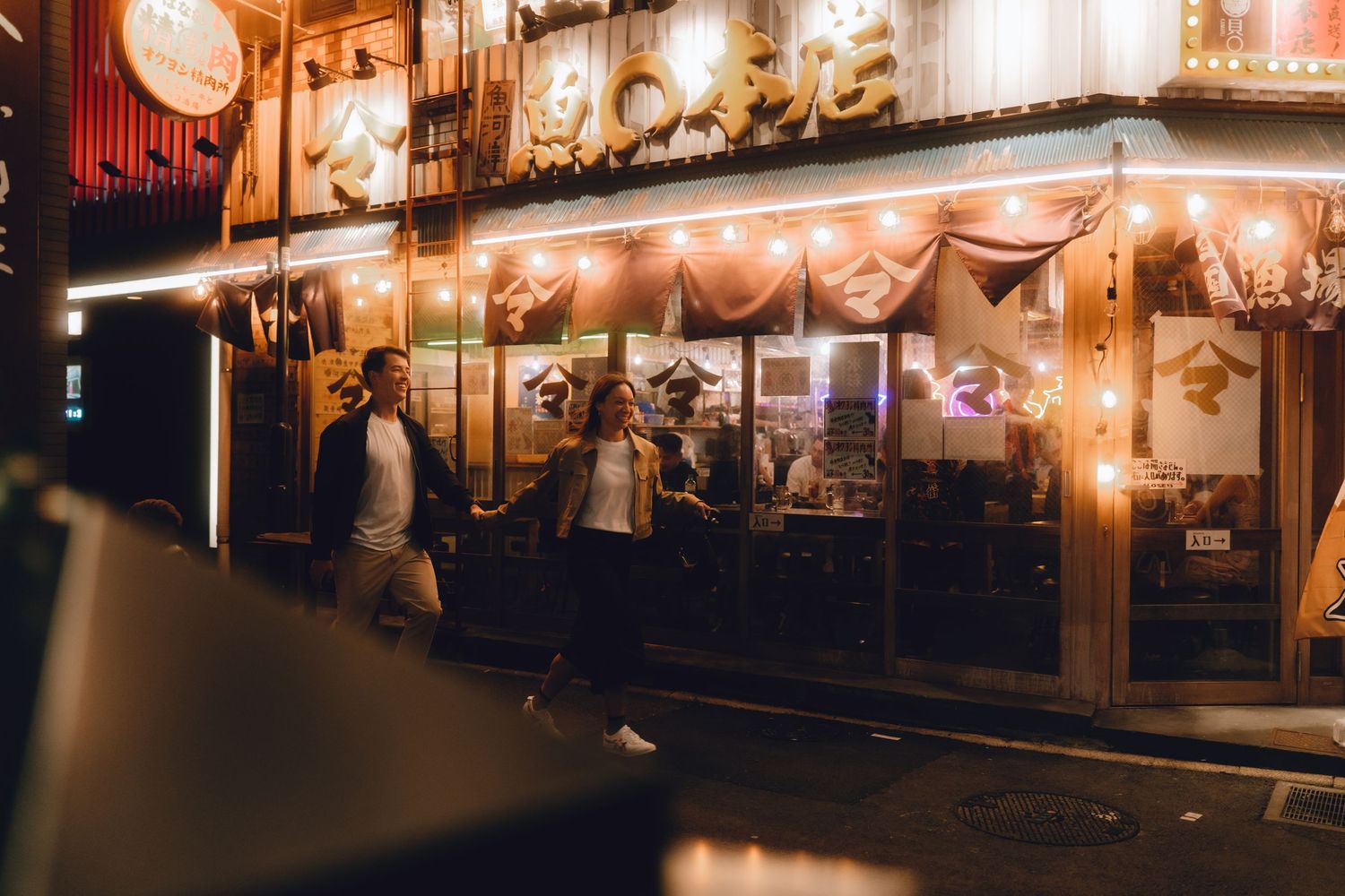 Couple strolling past a warmly lit traditional Japanese restaurant glowing at night in yurakucho, tokyo.