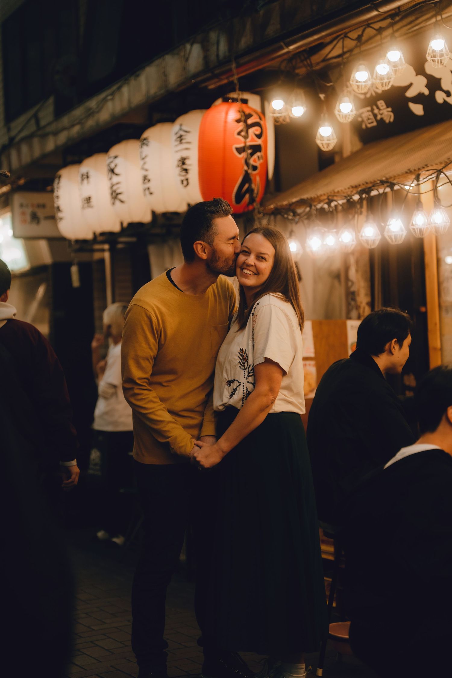 Couple sharing a romantic moment outside a Japanese restaurant at night, surrounded by glowing paper lanterns in tokyo.