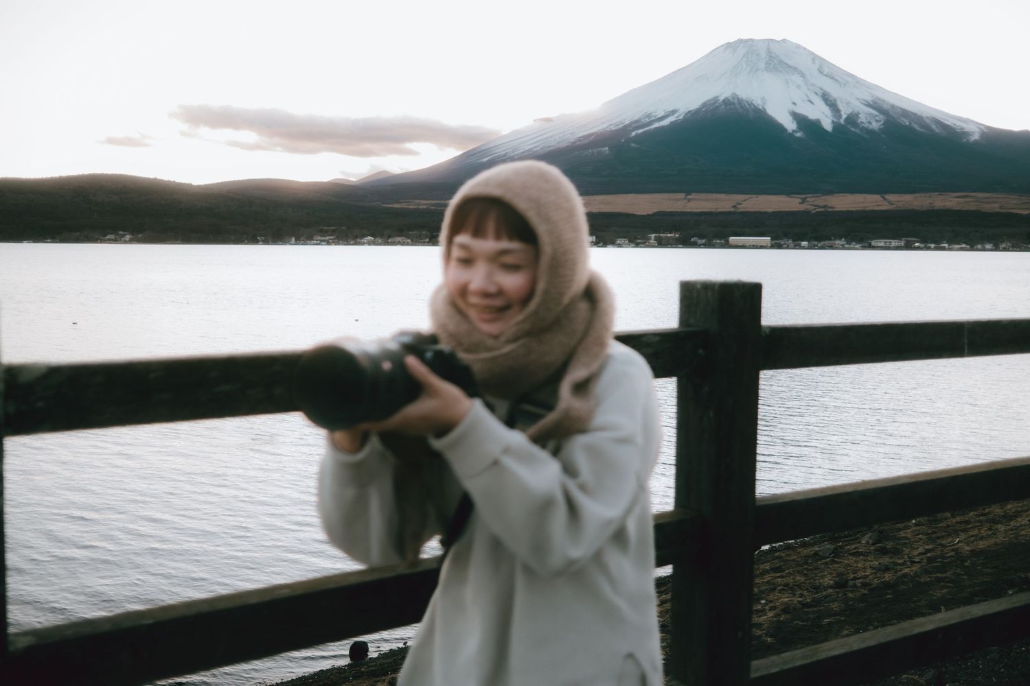 Happy woman checking camera at wooden fence with snow-capped Mount Fuji rising in lake yamanaka.