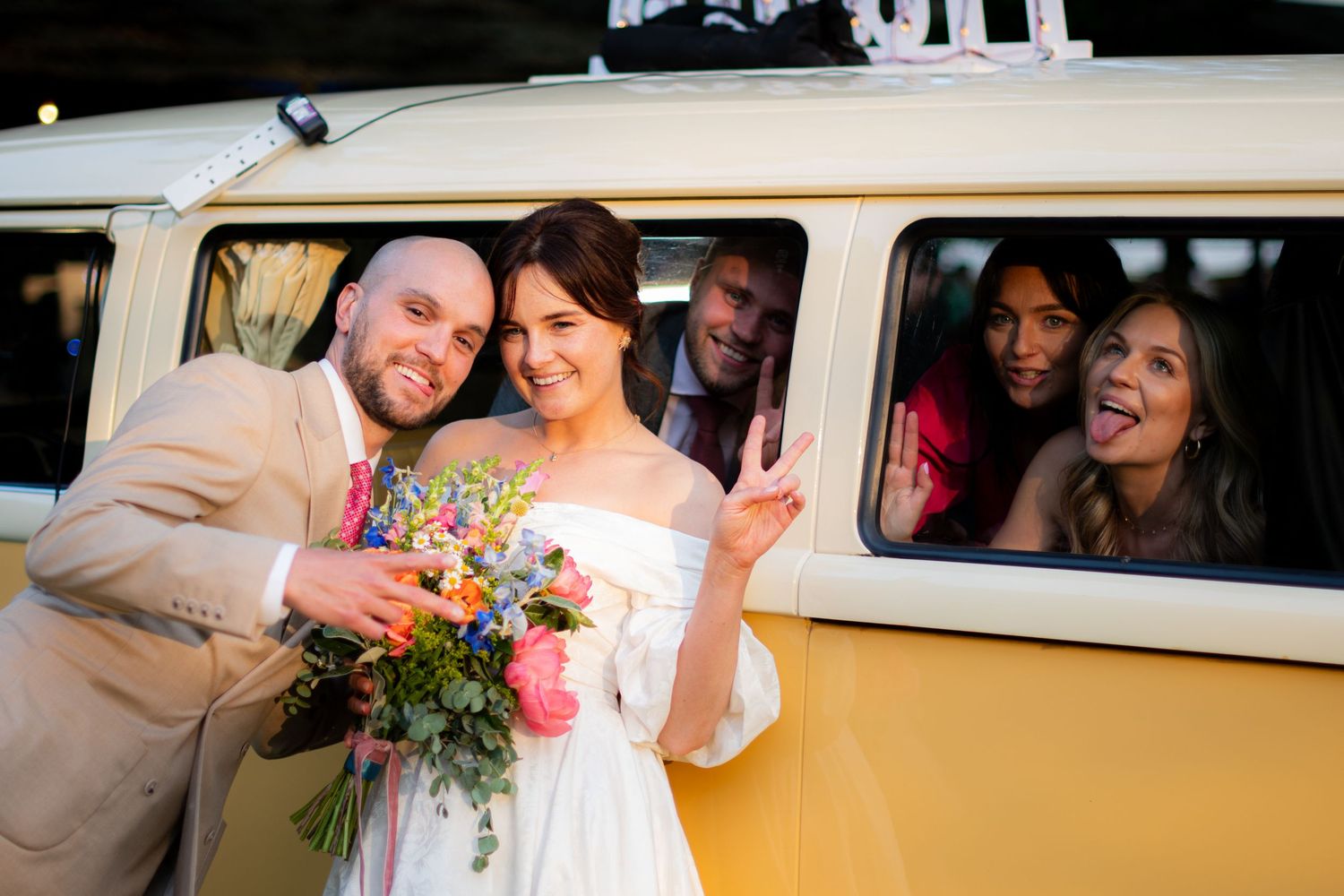 Portrait photo of the wedding couple posing in-front of their family, it is sharp with high contrast and a blurry background.