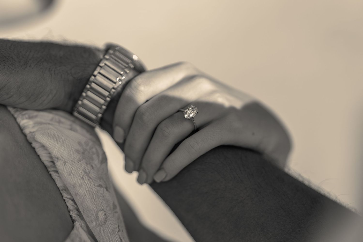 Sepia-toned close-up of a couple holding hands, woman wearing a diamond engagement ring and man wearing a watch.