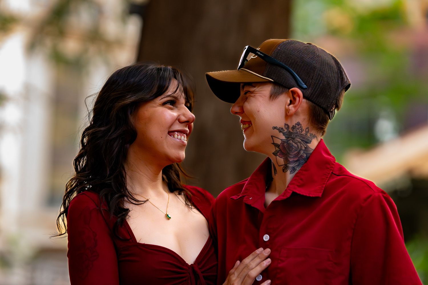 A smiling couple in red outfits share a joyful moment together on a sunny street.