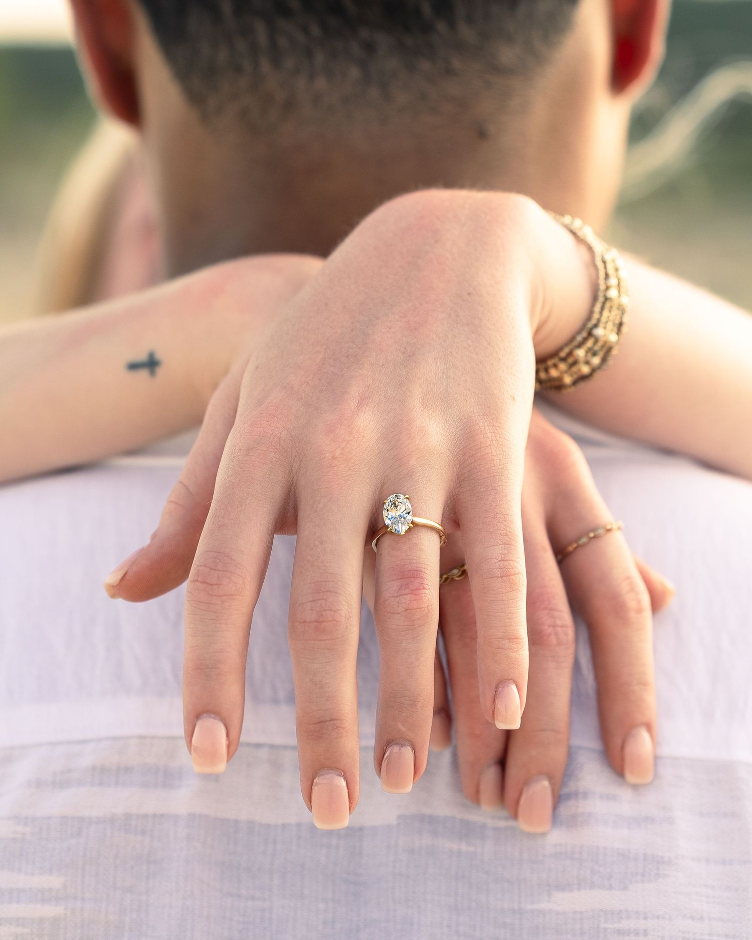 Close-up of a woman's hand displaying a solitaire diamond engagement ring while embracing a man.