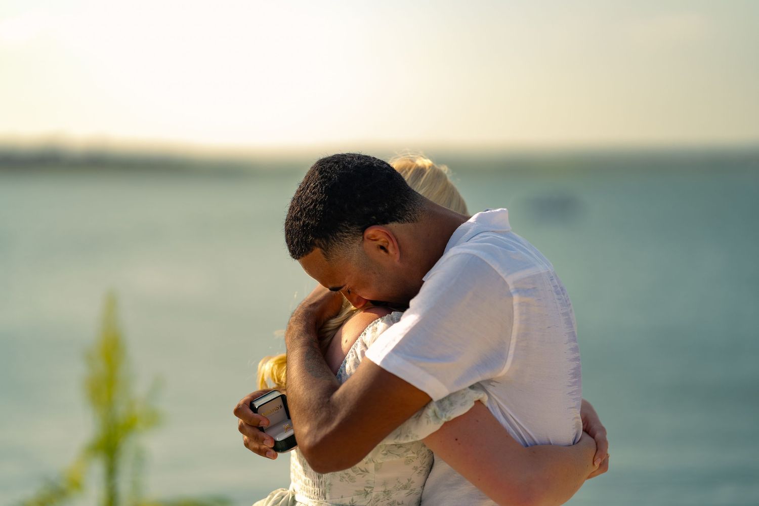 Couple embracing tenderly at sunset by the water, sharing an emotional romantic moment outdoors.