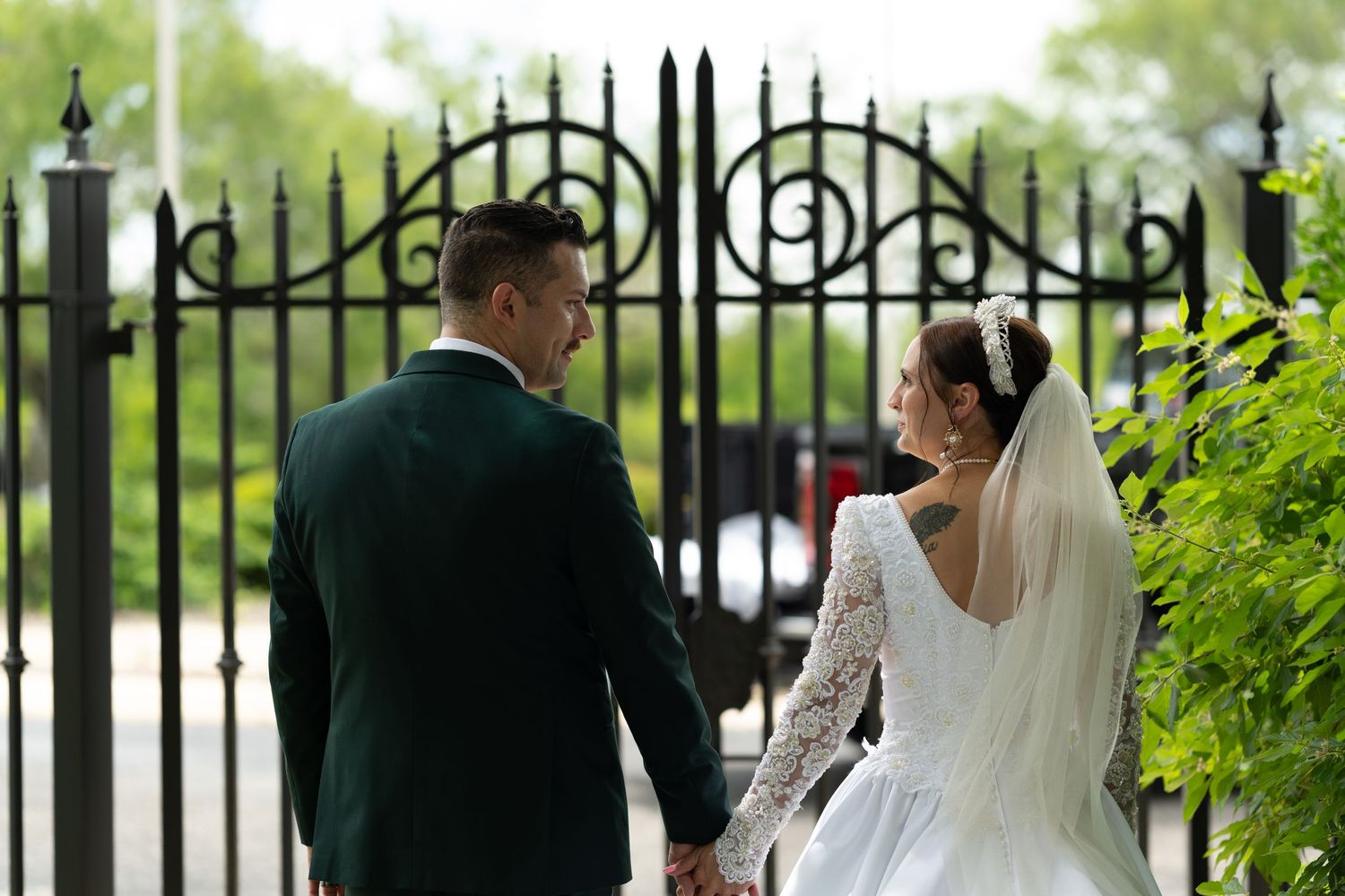 Bride and groom holding hands facing ornate black iron gates on their wedding day.