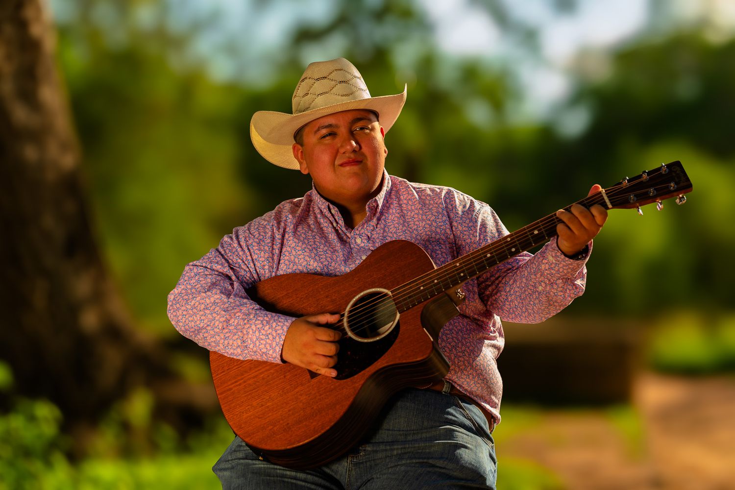Man in cowboy hat playing acoustic guitar outdoors in warm golden light.