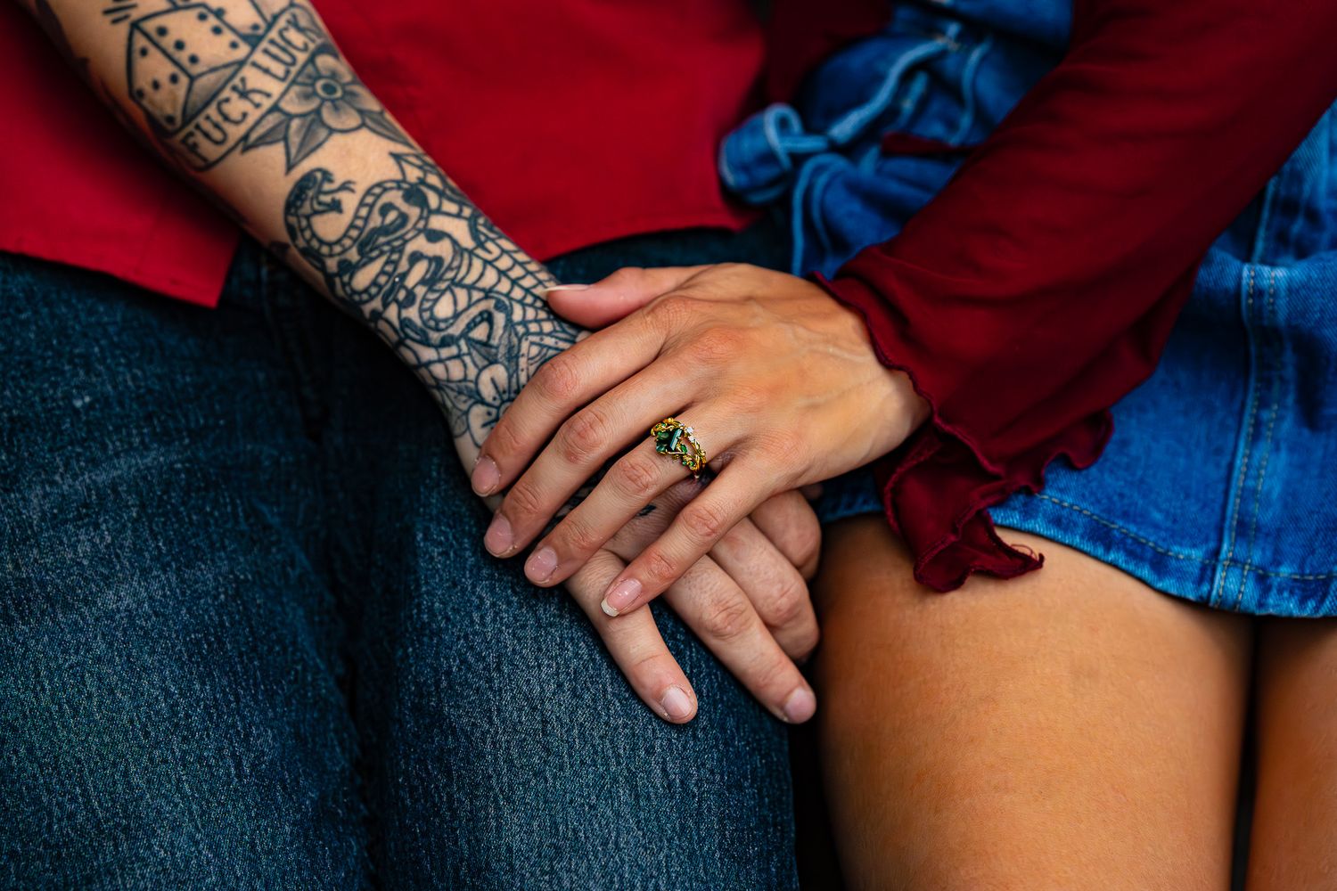 Close-up of two hands touching, one with a tattoo sleeve and green ring, wearing red and blue outfits.