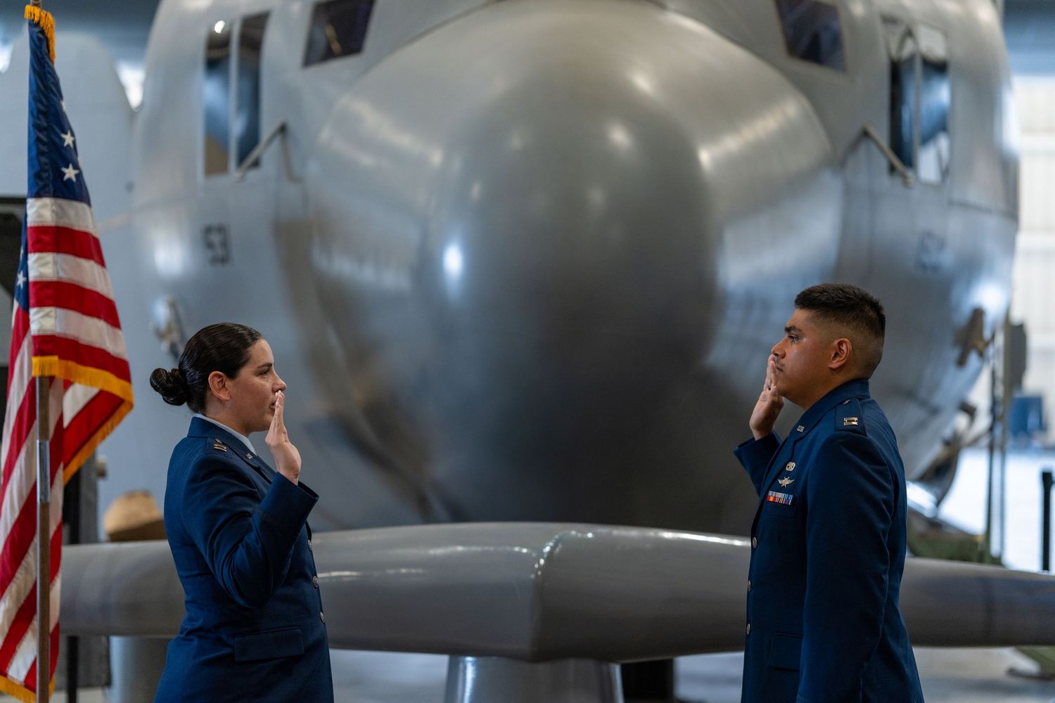 Two uniformed military officers reciting an oath before an aircraft exhibit.