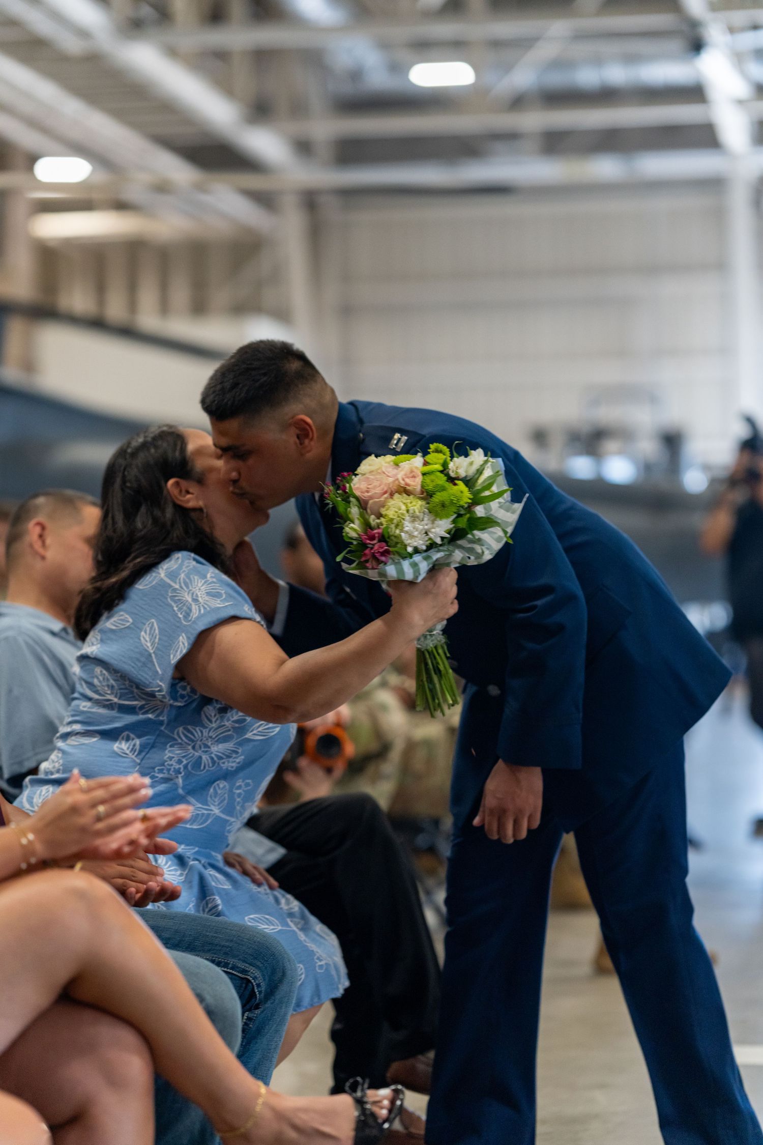 Military officer in dress blues kissing a woman while presenting her flowers.