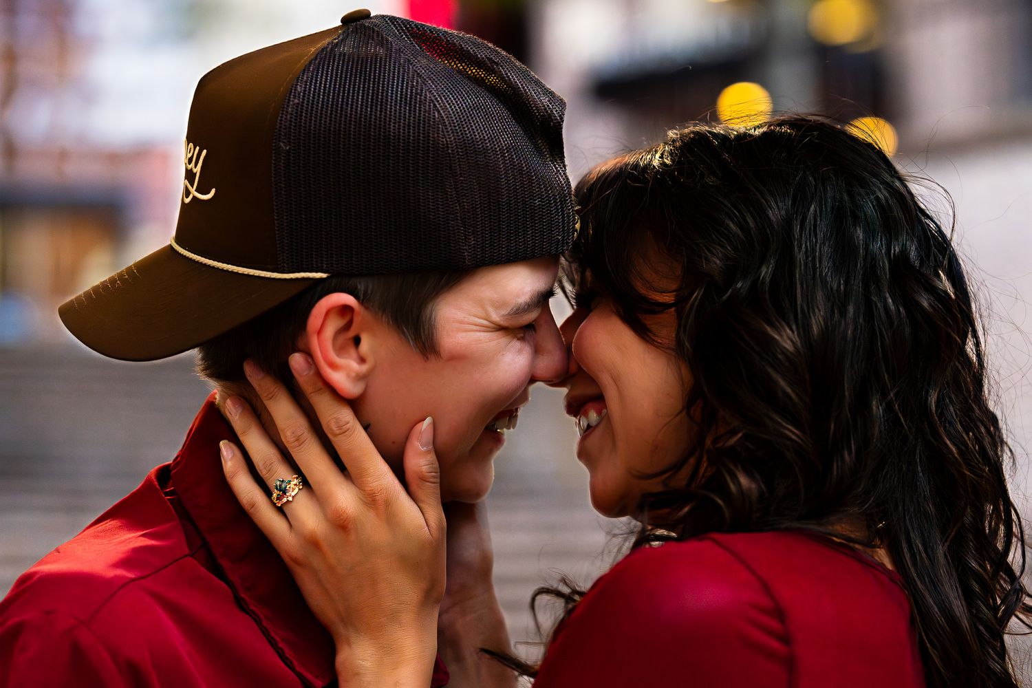 Couple sharing a tender romantic moment, nearly kissing, with bokeh city lights in background.