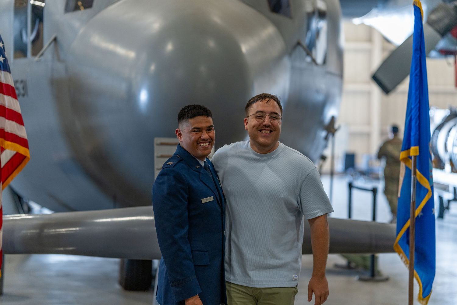 Two men smiling and posing together in front of a large aircraft display.