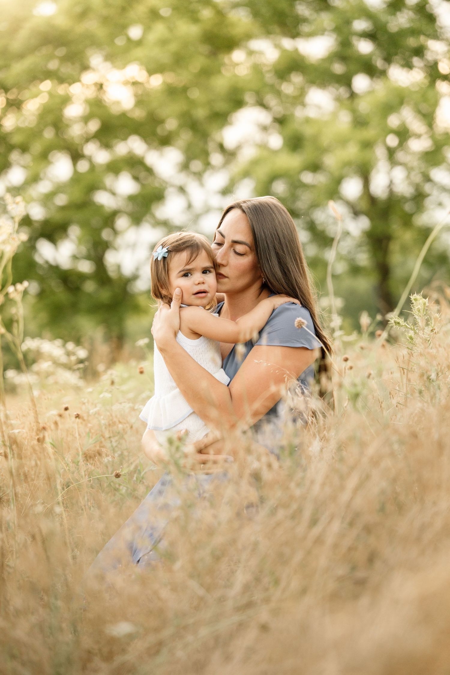 Loving mother kissing toddler daughter's cheek while holding her in a wildflower meadow.